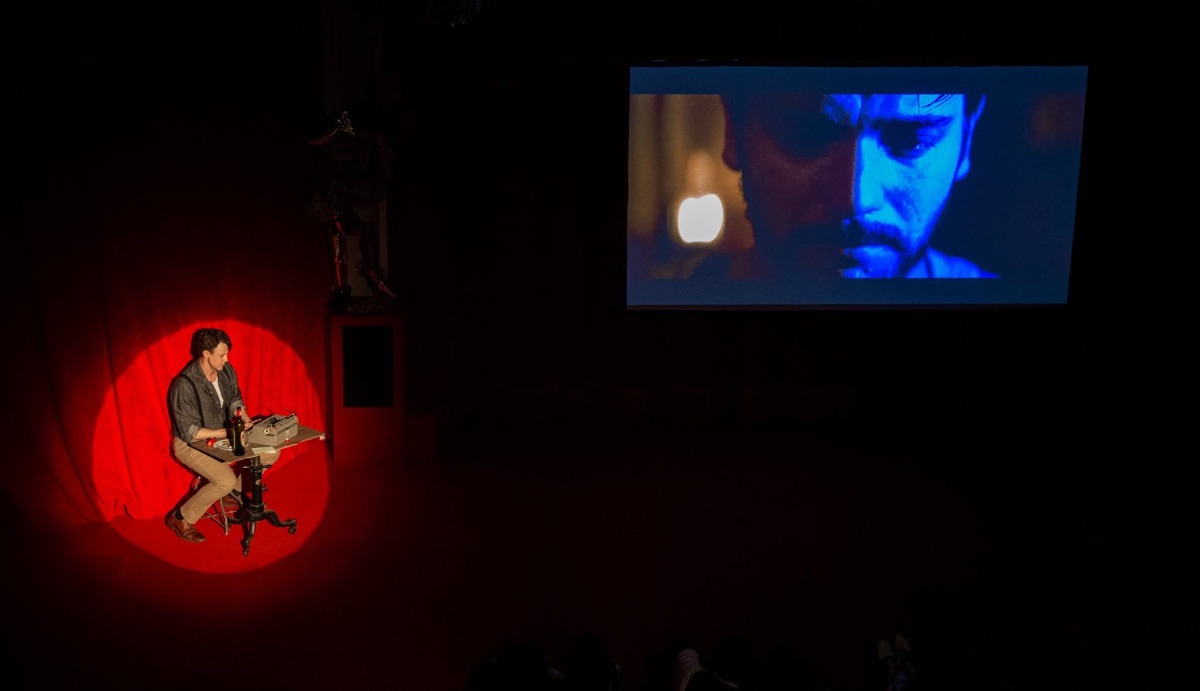 A performer in a red spotlight beside the screen